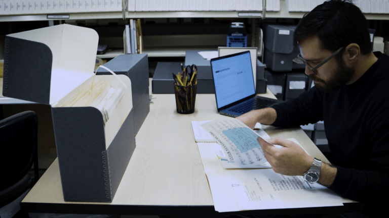 Gabriel Bouche Caro sits at a desk studying sheet music at the Silberman School of Social Work with his laptop nearby.